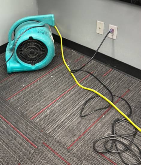 Teal air mover drying commercial carpet in an office