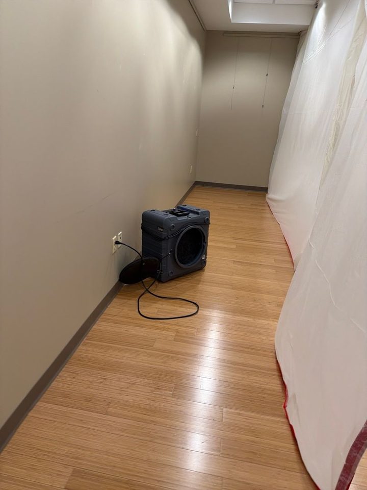 Air mover drying a hallway with a wood floor, next to a plastic containment wall, in a commercial building after a water loss